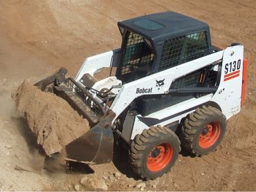 A skid steer in operation with bucket loaded with soil.