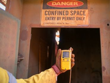 Holding a gas test monitor near a confined space to test for toxic gas.