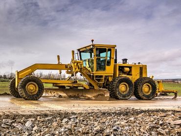 A large, yellow grader working on road.