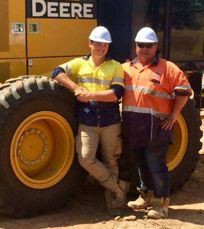Two workers wearing PPE standing in front of earthmoving machine.